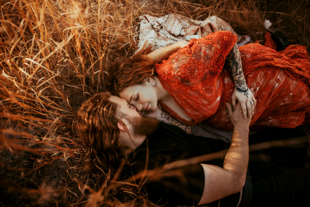 Husband and wife laying in Pine Barrens in NJ for maternity session with their heads together, eyes closed, and hands on belly. Mom was wearing a beautiful orange vintage lace gown. Sunset